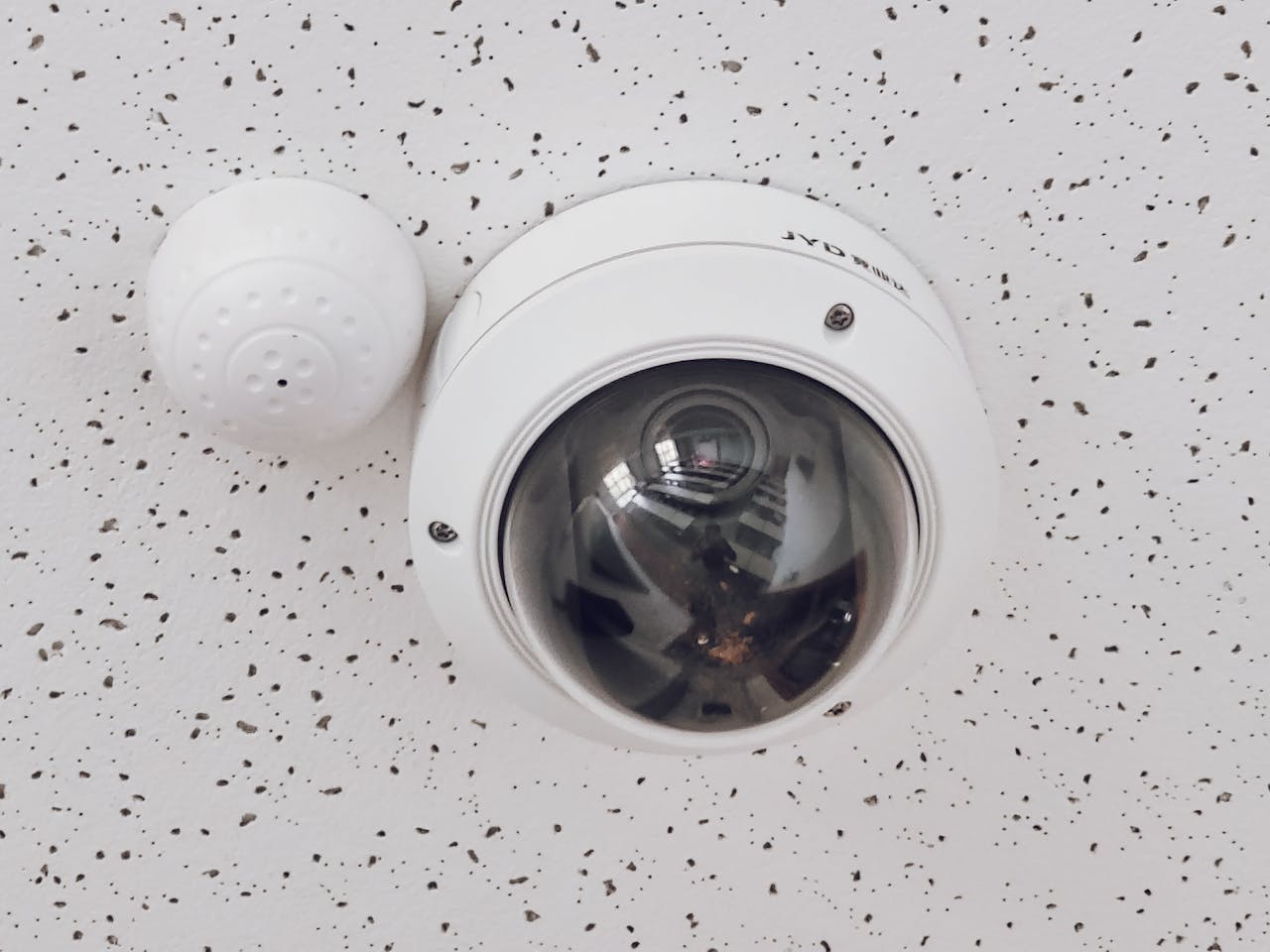 about-03 Close-up of a round dome surveillance camera installed on a speckled ceiling for security monitoring.